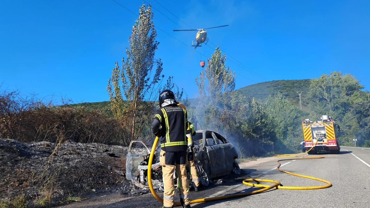 Bombero de Ponferrada con un helicóptero de apoyo apagando el fuego del vehículo calcinado.